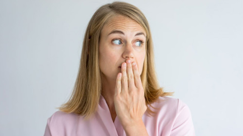 Woman covering her mouth with hand, looking anxious about Invisalign attachments at work